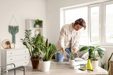 Handsome gardener with plants on table at home