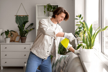 Handsome gardener watering plant on windowsill at home