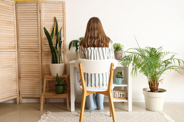 Young woman working at table with houseplants in office, back view