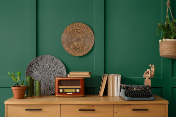 Vintage typewriter with books and radio receiver on commode near green wall in room