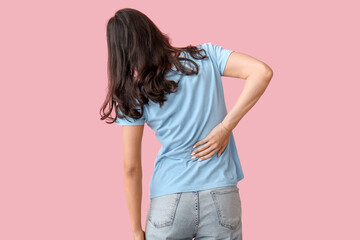Beautiful young woman suffering from back pain on pink background