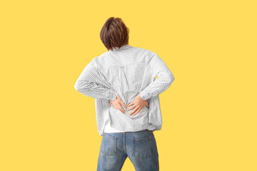 Handsome young man suffering from back pain on yellow background