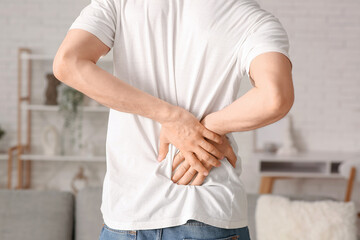 Handsome young man suffering from back pain at home, closeup