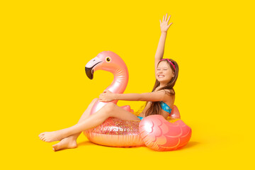 Cute little happy girl in swimsuit with inflatable ring and goggles sitting on yellow background © Pixel-Shot