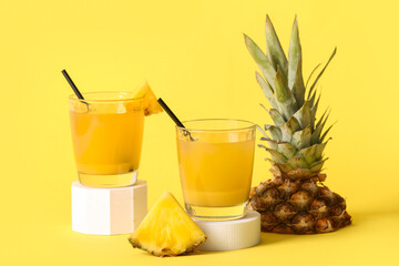 Glasses of fresh tasty pineapple juice on stands against yellow background