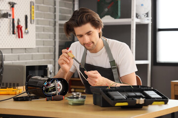 Male worker with soldering iron repairing coffee machine on table in workshop