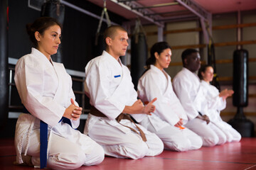 Group of multiracial people in kimono kneeling on floor during karate training.