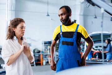 BIPOC mechanic helping client with car maintenance in auto repair shop. Employee in garage facility...
