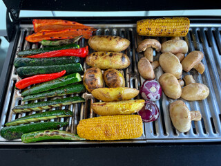 Assorted vegetables champignons mushrooms, potatoes, zucchini, corn and red onions on the grill directly above view