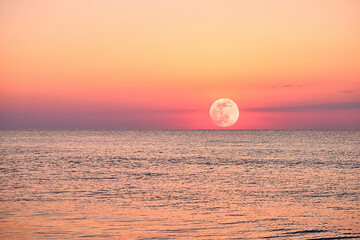 A vibrant moonlight the ocean, with a fiery sky and calm waters.