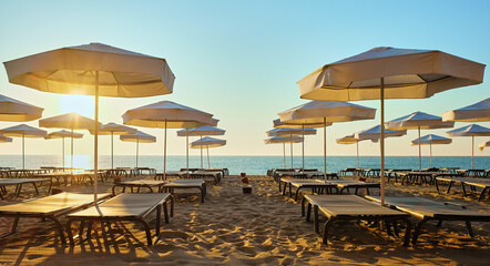 Relaxing on the beach. A row of white beach chairs and umbrellas on a sandy beach at sunrise.