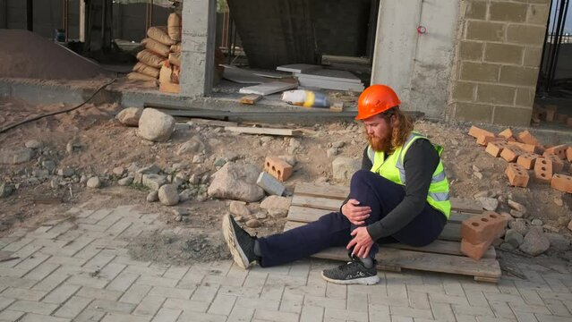 Male worker sitting on floor after accident in construction site. Injured builder worker who broke his leg while working. Copy space. Injury at work.