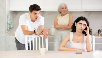 Domestic quarrel - offended young woman sits at the table while mother and young husband yell at her