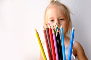 small child, blonde girl holds joyfully a bunch of colored pencils, concept of parenting, student...