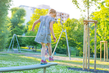 happy preschool girl walks on horizontal sports game playground equipment, child in rays light,...