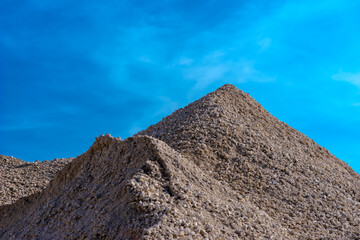 A pile of gravel looking picturesque against the blue sky background. A warehouse of construction...