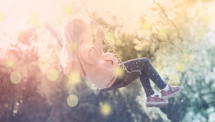 joyful little girl ascends into sunny sky on swing, blurred child figure in rays light, happy...