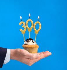 Hand delivering birthday cupcake - Candle number 300 on blue background