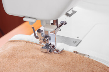 Modern sewing machine special presser foot with beige fabric and thread, closeup. Sewing process of...