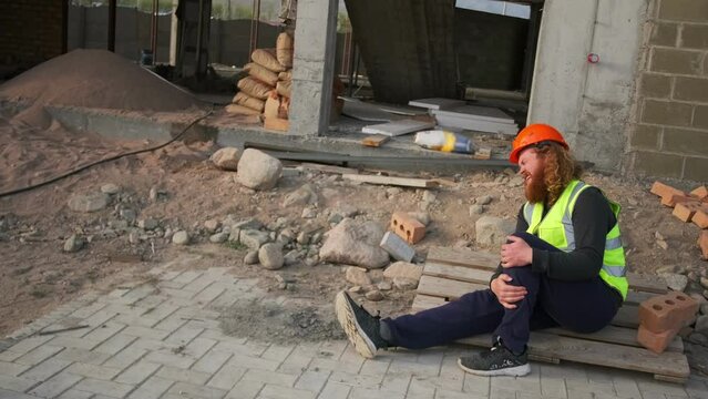 Accident of man worker at construction site is injured and in pain sitting on floor with broken leg. Injury compensation claim.