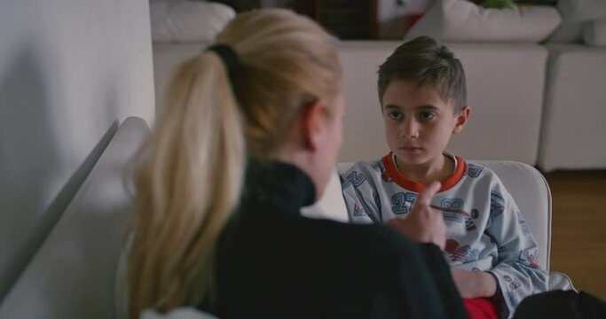 A mother is seen reprimanding her young son, who appears attentive and possibly remorseful, in the familiar environment of their home.