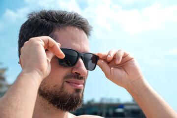 Young adult man taking off his sunglasses contemplating beautiful beach horizon