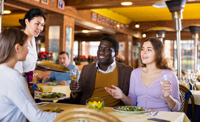 African-american man and Caucasian woman having dinner in restaurant with their female friend....