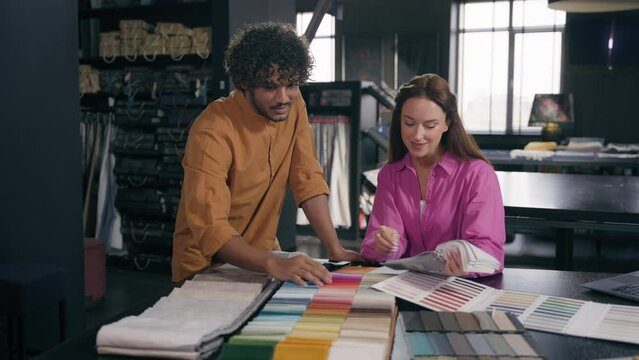 Diverse fashion designers Arabian man Caucasian woman couple customers choosing fabric samples talk discuss interior design salesman help to choose swatches colors material cloth in tailoring atelier