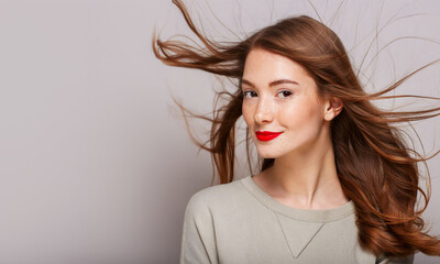 Elegant young woman with freckled and toussled red har, flying in the breeze wearing bright red lipstick. Copy space on left.