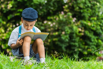 little Latino boy sitting in the park reading a book, very concentrated, looking at