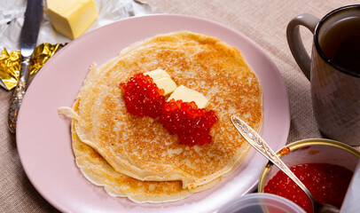 Delicious fried pancakes served with red caviar and piece of butter on plate
