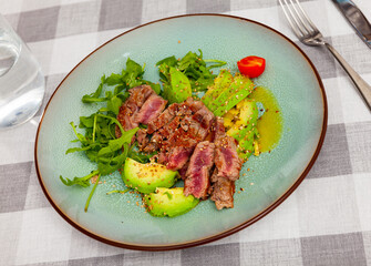 Appetizing roasted beef served with avocado and arugula on platter