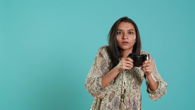 Competitive woman playing videogames with motion controlled controller, studio background. Indian Person participating in internet multiplayer racing game using gyroscope function on gamepad, camera A