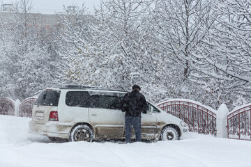 A man cleans the car from snow during a snowfall. Car parked in the snow. Lots of snow on the...
