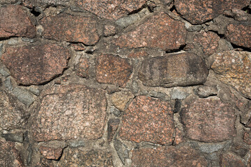 Ancient stone wall. Weathered rough surface of old masonry. Granite rock. Wall of a medieval castle. Vintage texture great for background and design.
