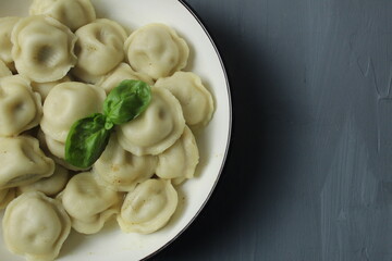 Cooked boiled dumplings in a bowl of basil greens top view close-up on a gray background with space for text copyspace