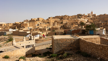 Dilapidated stone houses stacked on hillside in ancient Berber settlement of Tamezret with mosque...