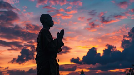 Silhouette of a monk in prayer against a colorful sunset sky, reflecting on the significance of Buddhist holy days.