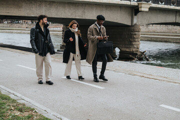 A group of three diverse business professionals walking together on a city riverside path, exuding confidence and teamwork in an urban setting.