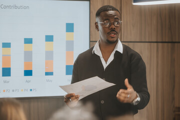 A young, professional businessman discusses growth statistics and company contributions during a meeting in a contemporary office setting.