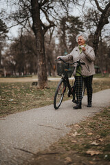 Mature woman standing with her bicycle in the park, exuding health and vitality during a leisurely break.