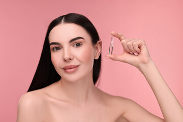 Beautiful young woman holding skincare ampoule on pink background