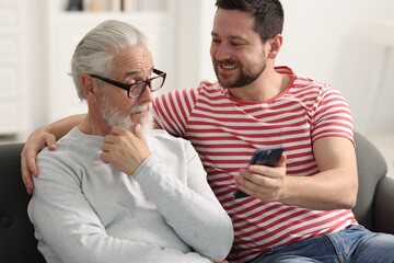 Happy son and his dad watching something on smartphone at home