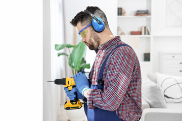 Young worker in uniform using electric drill indoors