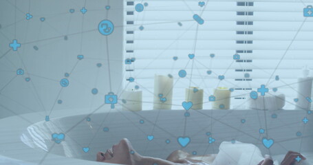 Image of network of digital icons over biracial woman relaxing in a bathtub in bathroom