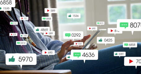 Image of social media icons over mid section of a woman using digital tablet at home - Powered by Adobe