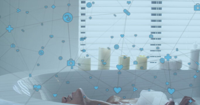 Image of network of digital icons over biracial woman relaxing in a bathtub in bathroom