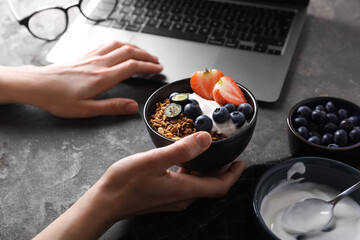 Woman with tasty granola at workplace, closeup