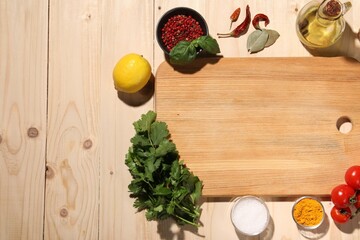 Cutting board surrounded by spices, tomatoes, oil and lemon on wooden table, flat lay. Space for text