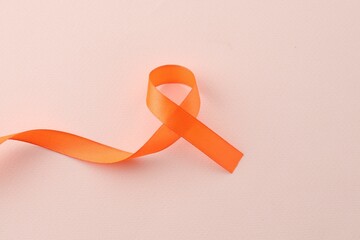 Orange awareness ribbon on beige background, top view